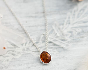  A playful 18" sterling silver necklace with a 10mm Baltic amber oval pendant on a light wood table, surrounded by soft decor. 
